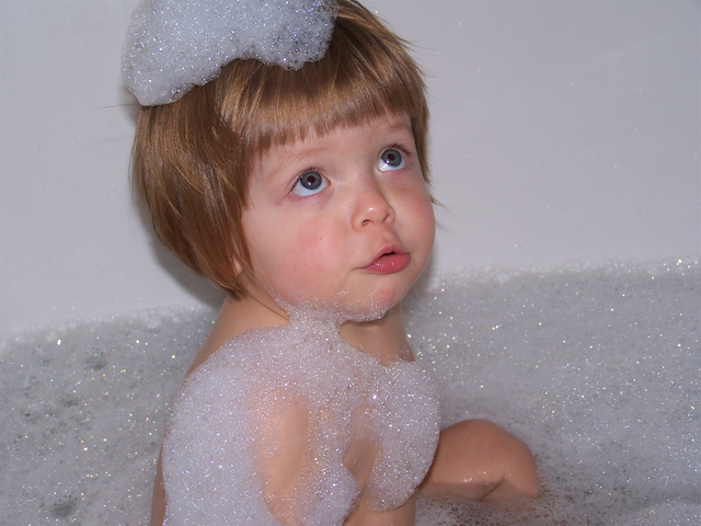 dítě sedící ve vaně s pěnou na hlavě